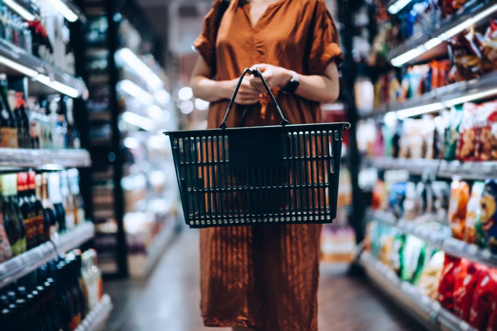 Woman with a shopping basket stands in supermarket aisle