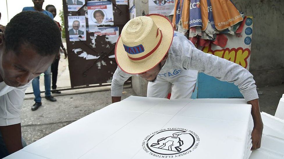 Люди несут избирательные материалы, доставленные Временным избирательным советом (ВИС) за день до всеобщих выборов на избирательном участке в центре Порт-о-Пренса, 19 ноября 2016 г.