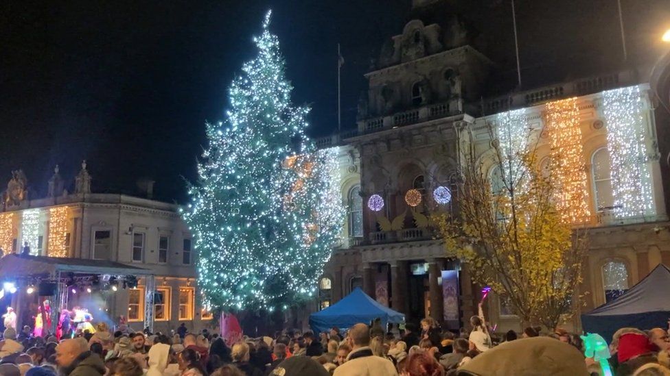 Large crowd in front of Christmas tree with lights turned on