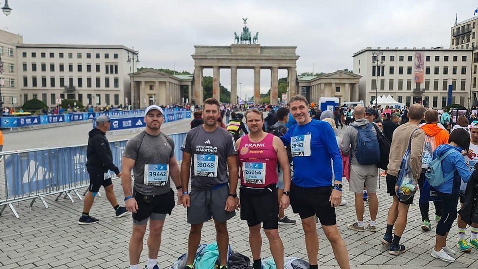 Four men in running gear in a crowd in central Berlin.