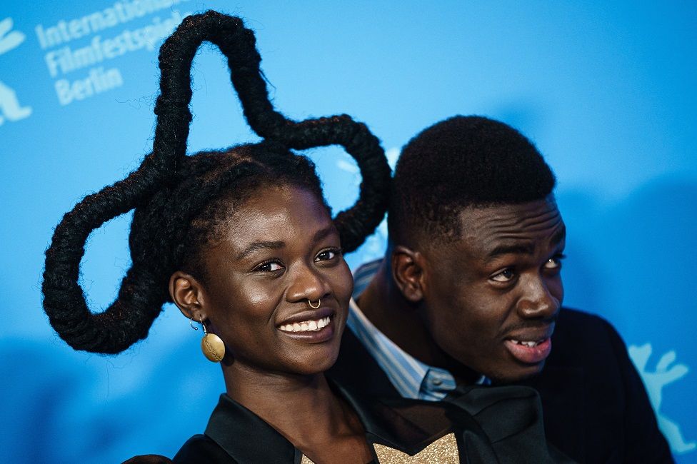 A woman with an elaborate hairstyle poses on the red carpet with a man.