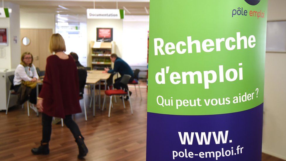 A woman walks next to a board that reads "Looking for a job, who can help you?" in a branch of France's national employment agency Pole Emploi