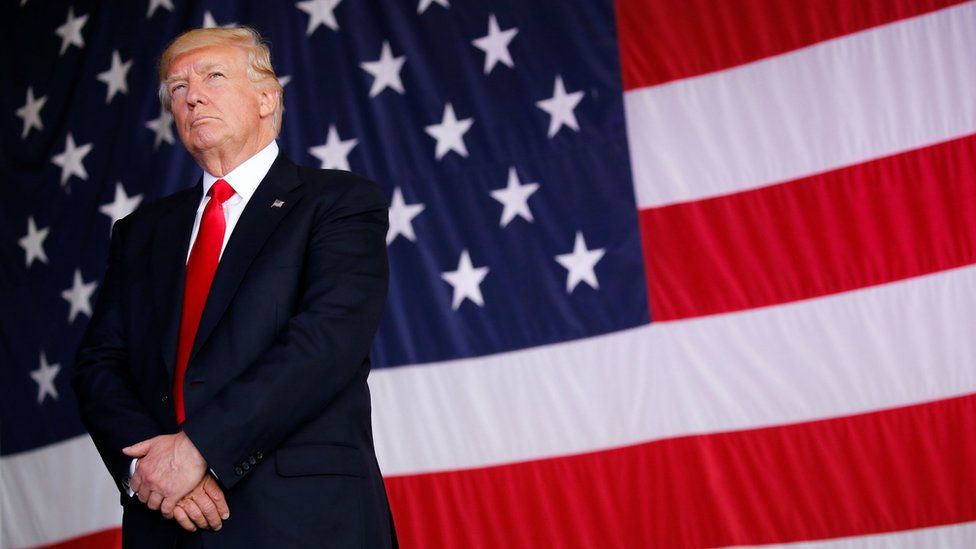 US President Donald Trump stands in front of American flag