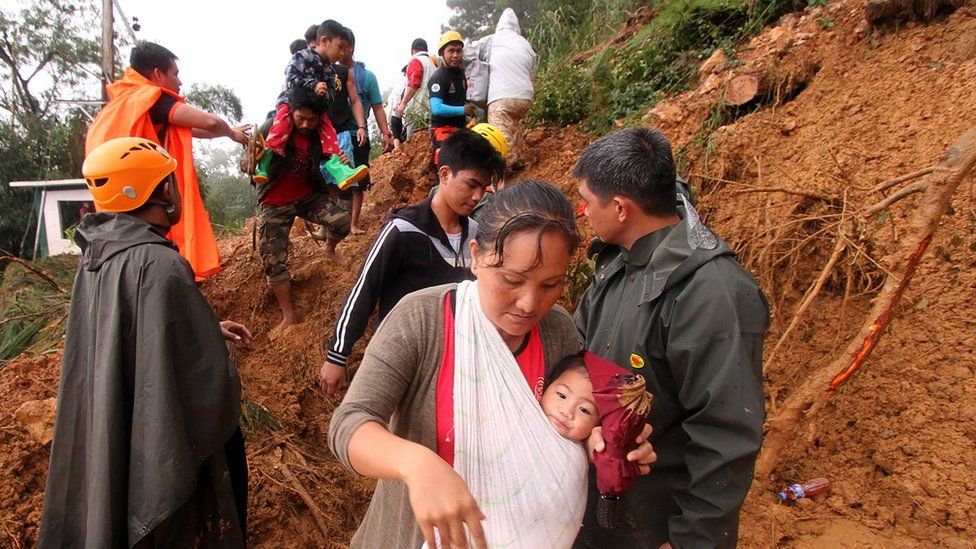 People carrying children climb over muddy landslides in Itogon