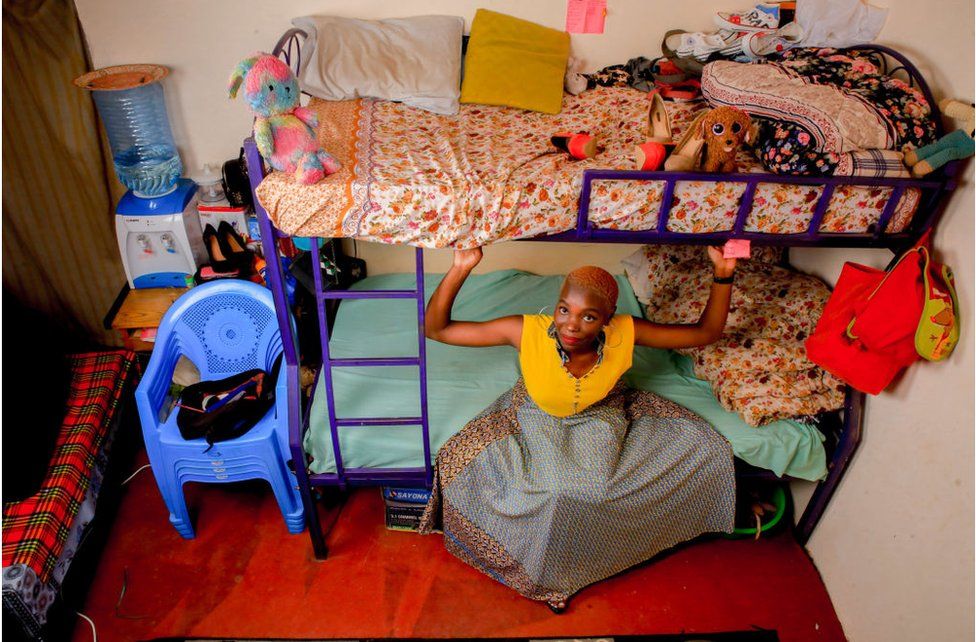 Woman in skirt sitting on the bottom rung of a bunkbed in a bedroom.
