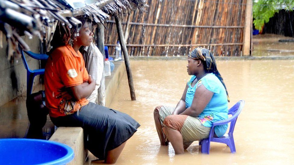 Neighbours chat while sitting in a flooded street of the Paquite district of Pemba