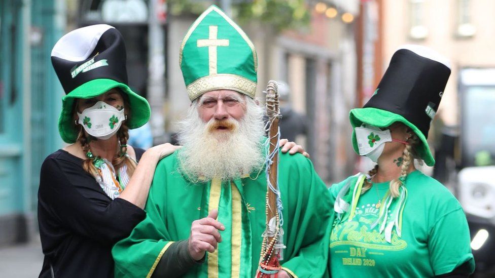 St Patrick beside two women wearing masks with shamrocks