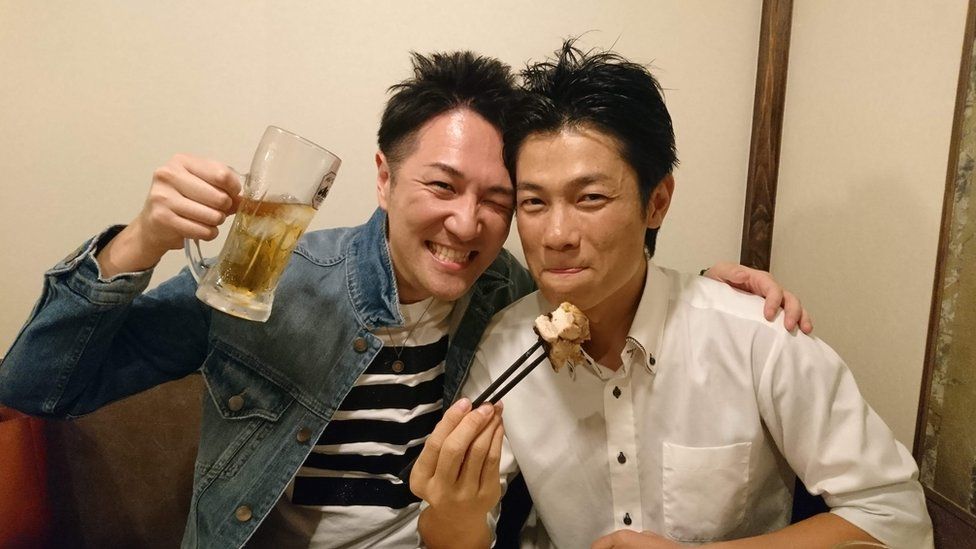 Yuichi Ishii levanta um copo de cerveja abraçado a um amigo