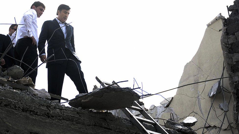 Georgian President Mikheil Saakashvili (C) sees the ruins of a building destroyed by a Russian bombing in Gori on 25 August 2008.