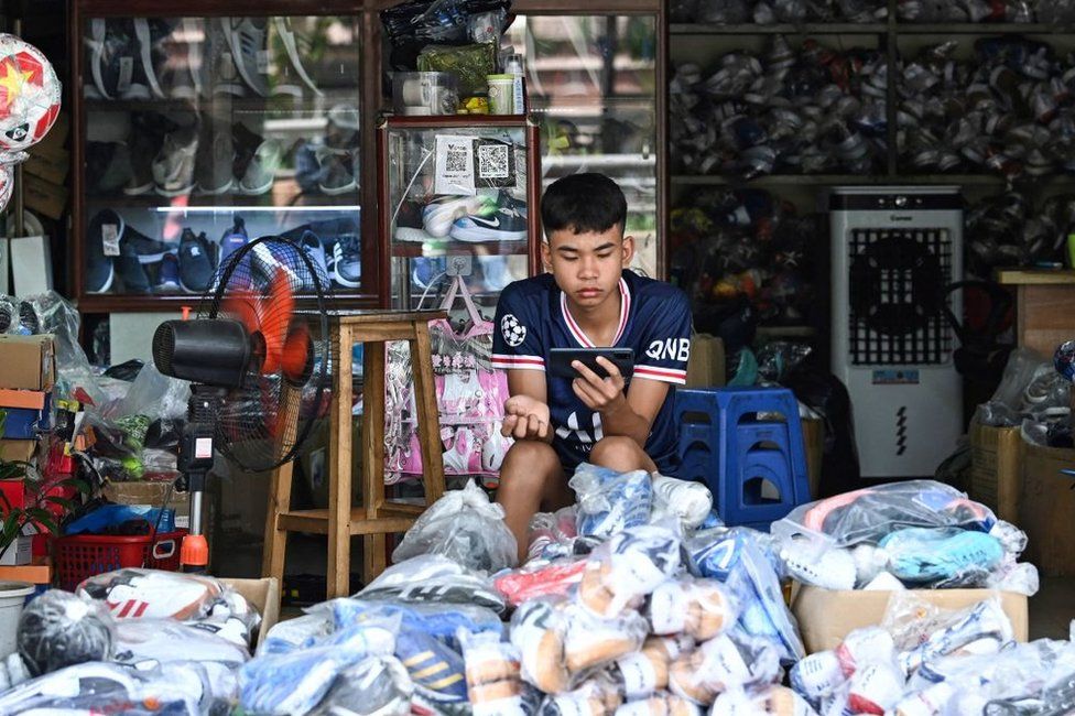 A young man uses his mobile phone as he waits for customers in a sports shop in Hanoi on June 20, 2023.