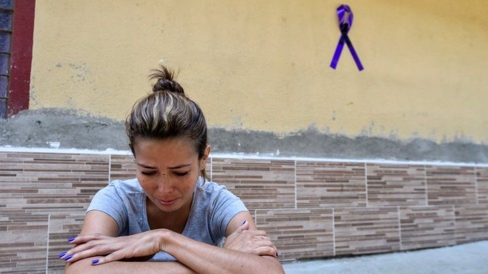 A relative of a victim of the Ecuador bus crash sits in front of a house with a ribbon