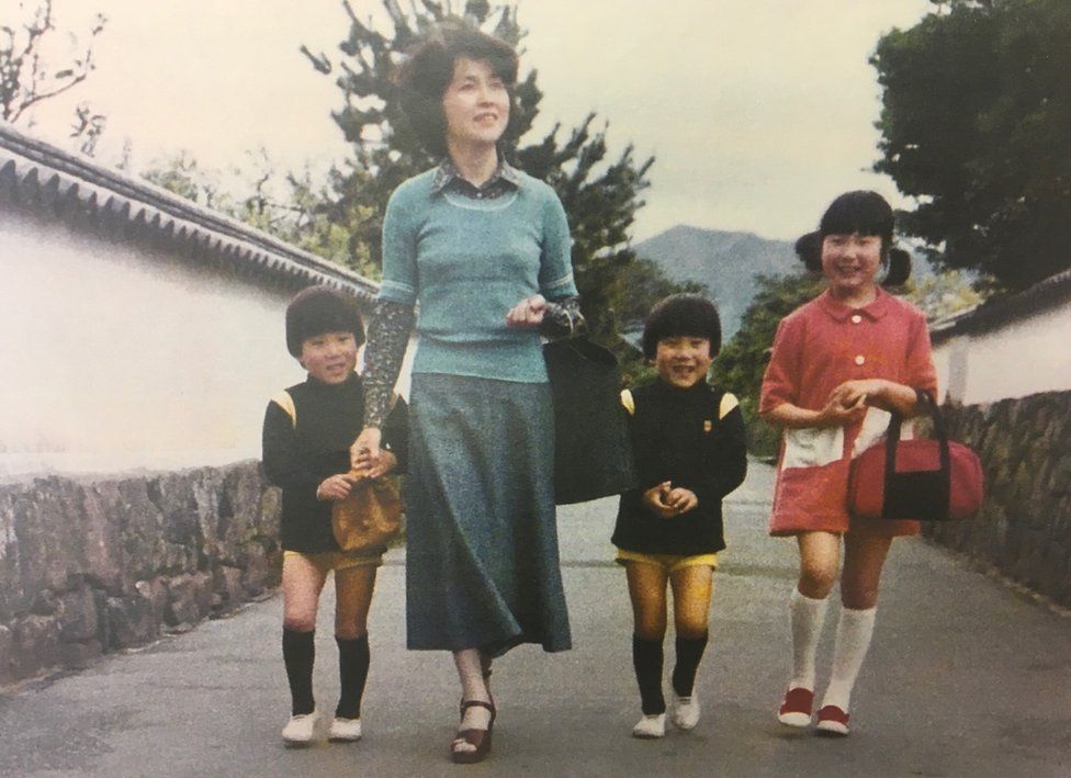 A picture showing a young Sakie Yokota and her three children when they were little, smiling as they walk down a street