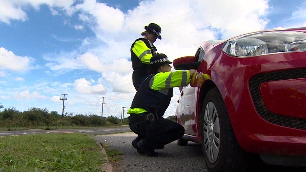 Police officers with a red car at the side of a road