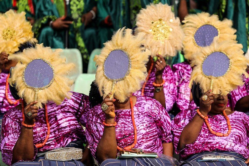 Women cover their faces with stitched, feathered fans.