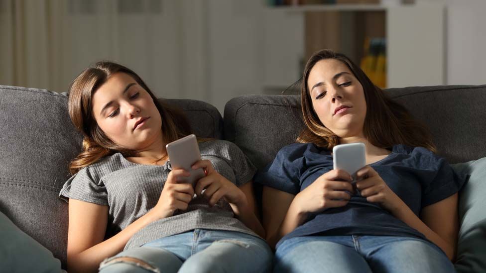 Two young women slouching and using their phones