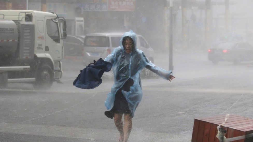 A woman runs in a waterproof with an umbrella in hand in heavy rainstorm in Shenzhen