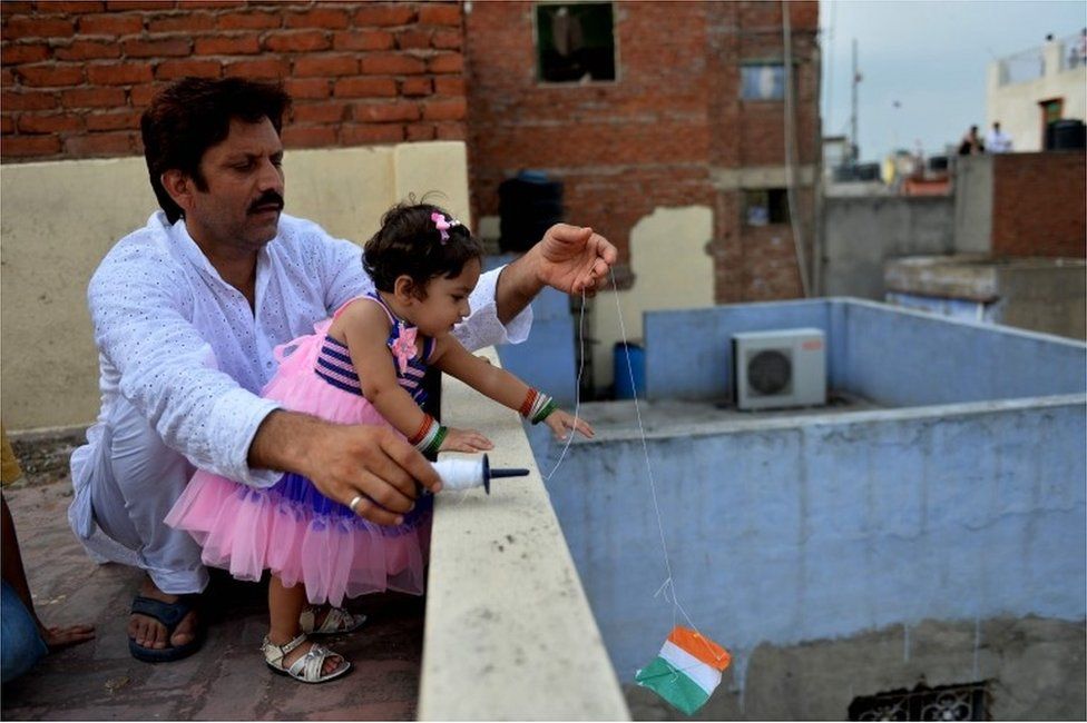 На этой архивной фотографии, сделанной 15 августа 2014 г., изображены отец и дочь из Индии, запускающие воздушных змеев со своей крыши во время празднования Дня независимости страны в старых кварталах Нью-Дели.