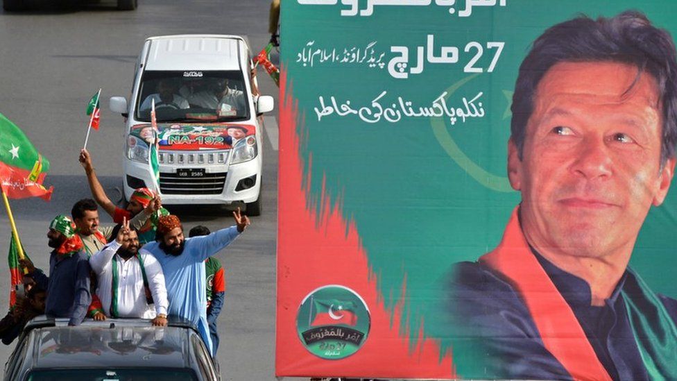 Activists and supporters of ruling Pakistan Tehreek-e-Insaf (PTI) party arrive to attend a rally next to a billboard with a picture of Pakistan's Prime Minister Imran Khan, in Islamabad on March 27, 2022.