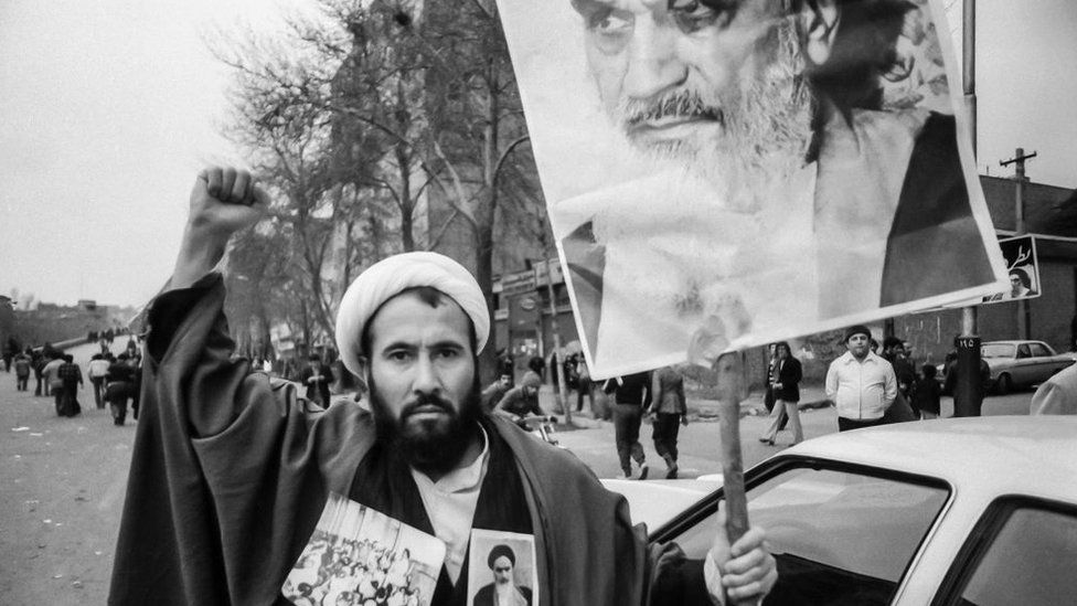 A Shia cleric holds up a banner showing Ayatollah Ruhollah Khomeini during Iran's 1979 Islamic Revolution
