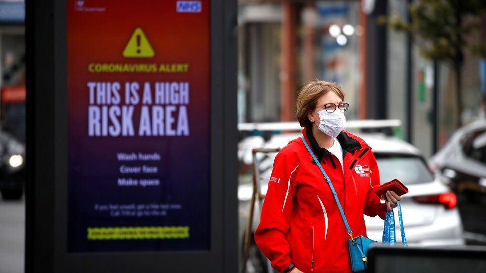 A woman wearing a protective mask walks past a warning sign in Manchester, as the city and the surrounding area faces local restrictions in an effort to avoid a local lockdown being forced upon the area, amid the coronavirus disease