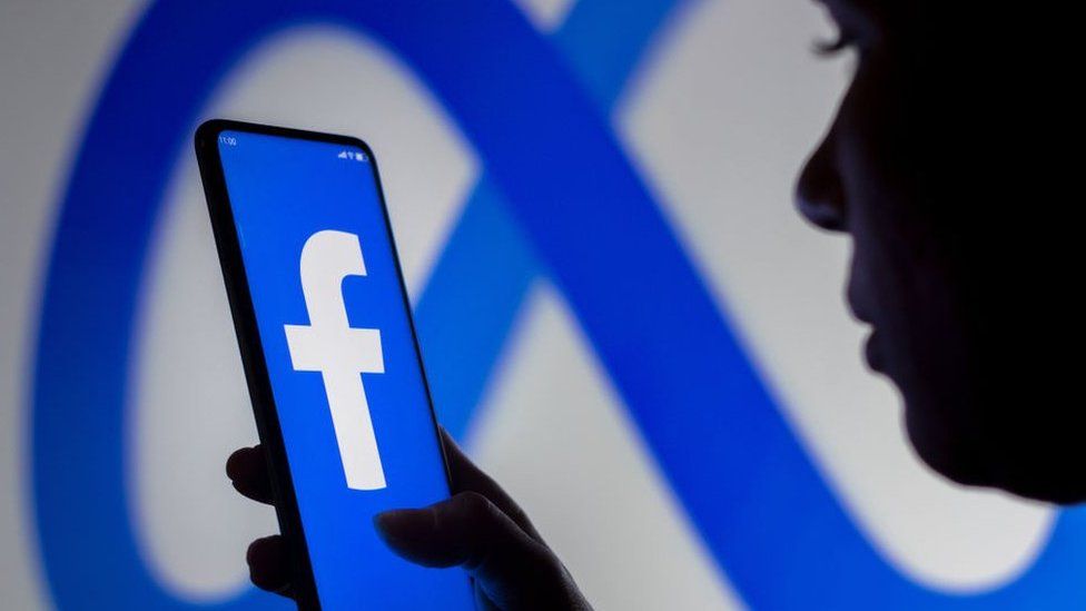 Person holds a smartphone displaying the Facebook logo against a Meta logo background