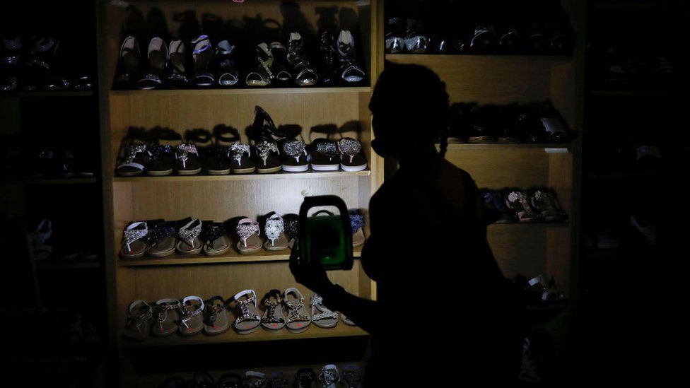Женщина использует перезаряжаемый светодиодный фонарь для освещения полка для обуви в Претории, 16 февраля 2023 г.