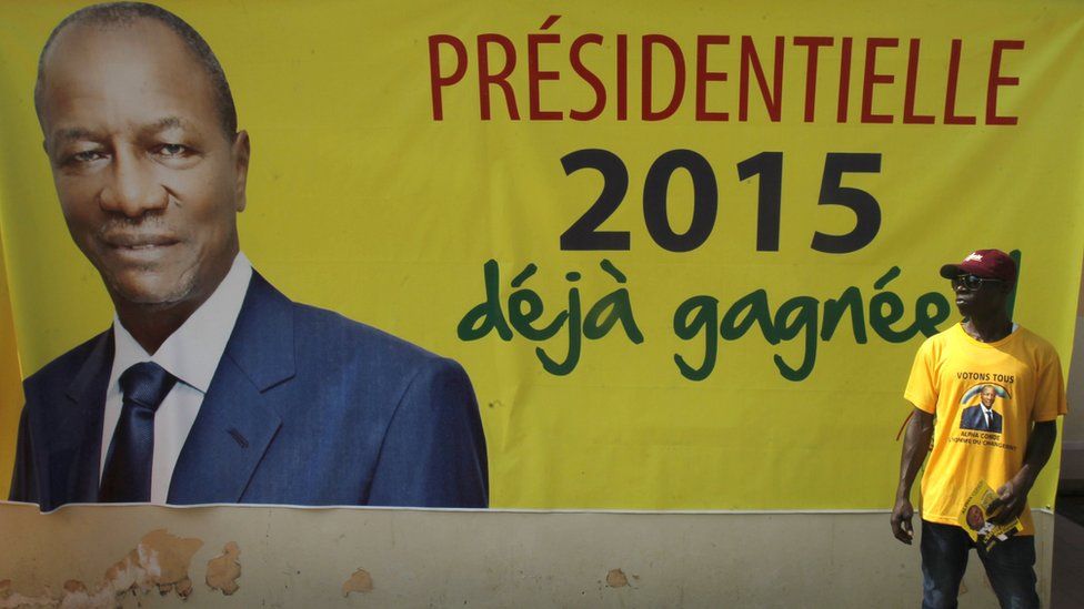 A supporter of Guinea's incumbent president and presidential candidate Alpha Conde stands in front of his campaign banner