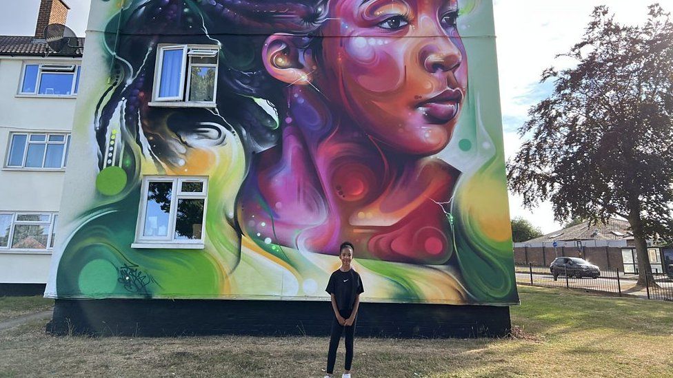 Nylah stands in front of a giant mural of herself on a house