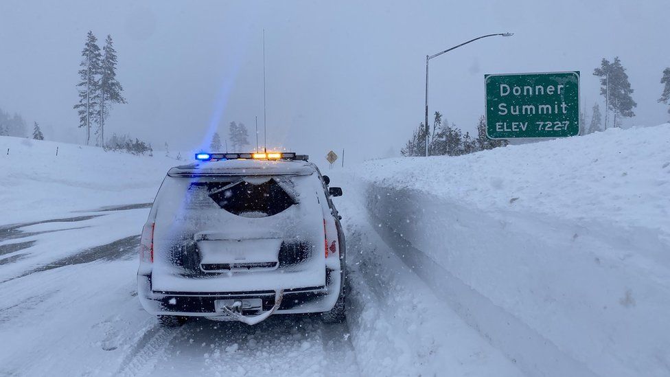 A California Highway Patrol car drives through heavy snowfall on the Nevada state line