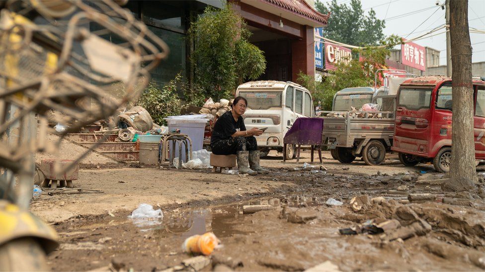 Woman sits surrounded by flood debris