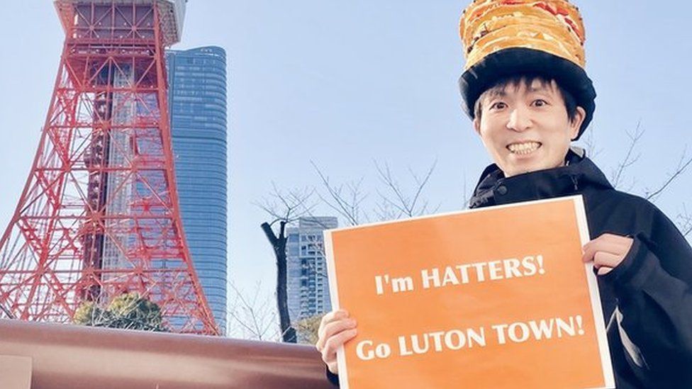 Sweets Nanako holding a sign that says "I'm Hatters, Go Luton Town" outside Tokyo tower
