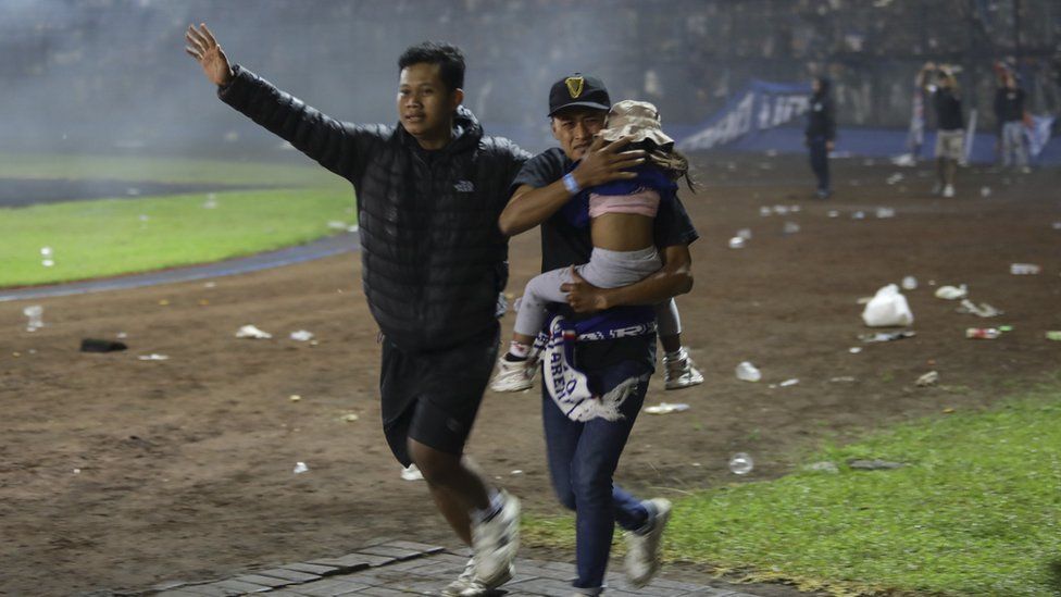Two men - with one carrying a child - run down the field to get away from the tear gas