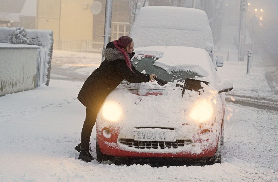 A woman clears snow from her car in Tow Law, County Durham, as Storm Eunice sweeps across the UK on 18 February 2022
