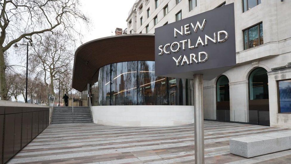 Glass-fronted entrance to New Scotland Yard, with the rotating sign in the foreground