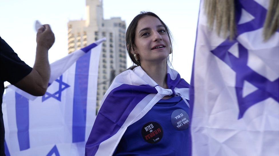A young woman draped in the flag of Israel participates in a pro-government rally
