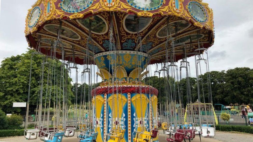 Carousel-type ride with chairs on chains. Trees and grass visible in the background.