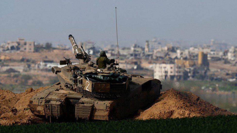 An Israeli tank manoeuvres along Israel's perimeter with northern Gaza, seen in the background (30 January 2024)