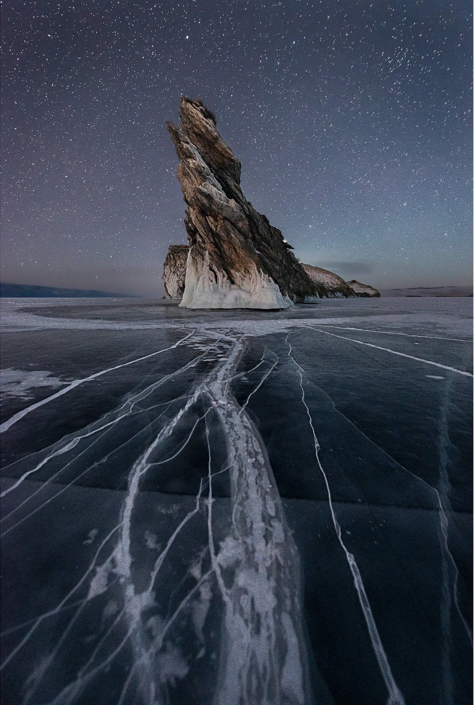 A steep rocky island protrudes out of a frozen lake