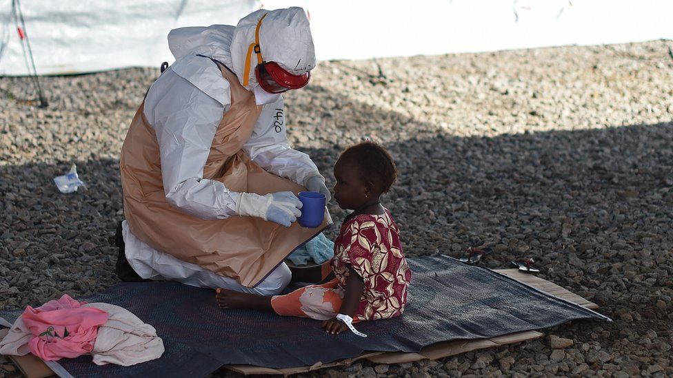 A child being fed by a medical worker in a protective suit