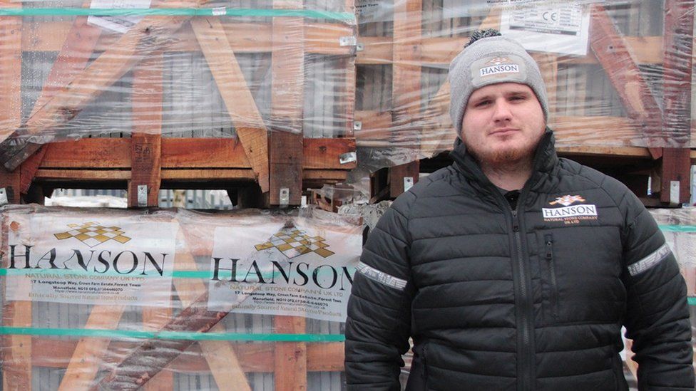 Ben Charlton standing before a stack of pavers in pallets