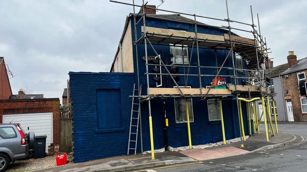 A house, painted dark blue, surrounded by scaffolding