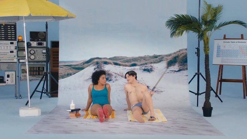 Женщина и мужчина сидят на пляжном полотенце в купальных костюмах