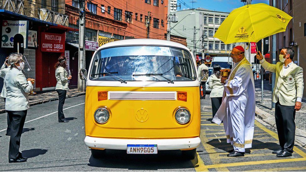 A cardinal from the Basilica Cathedral in Brazil wears a face shield as he gives communion in a drive-through ceremony during an Easter Sunday service amid the coronavirus pandemic in Curitiba, Brazil, 12 April 2020