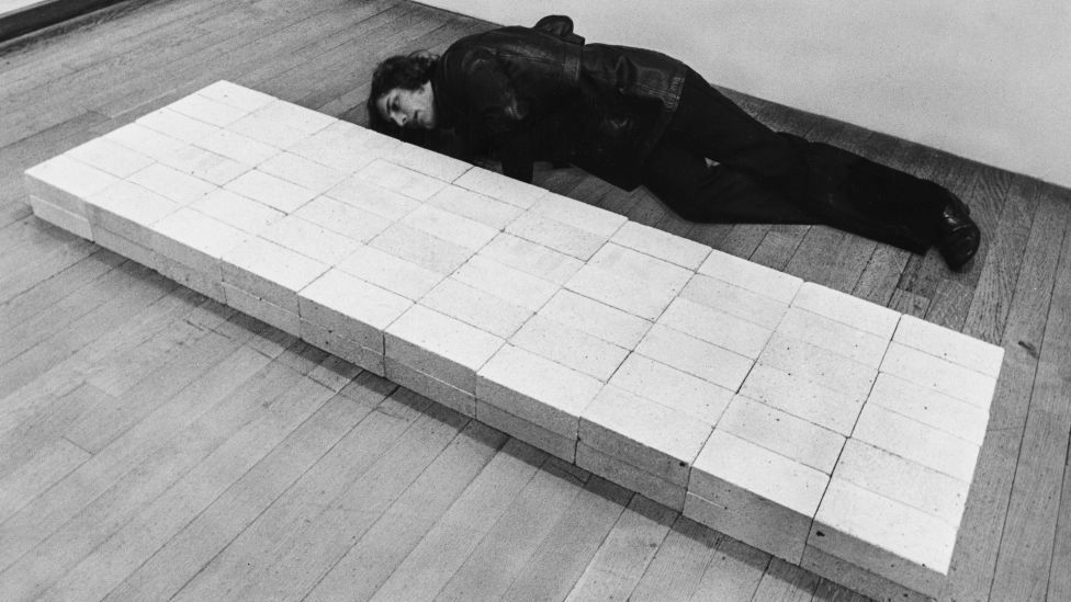 A man lies on the floor for a closer inspection of Carl Andre's 'Bricks' sculpture
