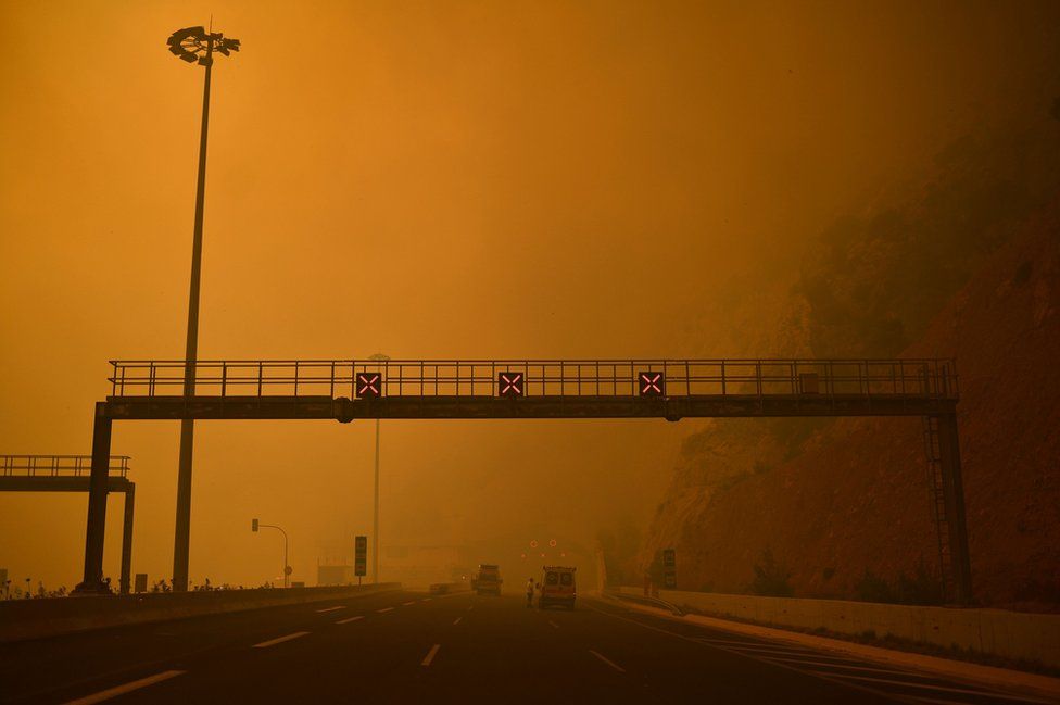 A road block is set up amid smoke as a wildfire burns in Kineta, near Athens, on July 23, 2018