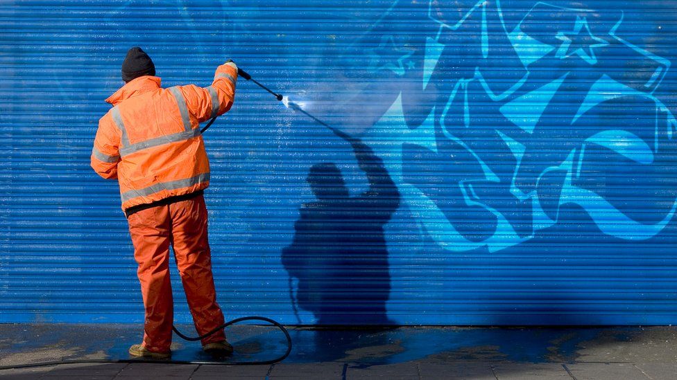 Man in hi-vis washes graffiti off garage door