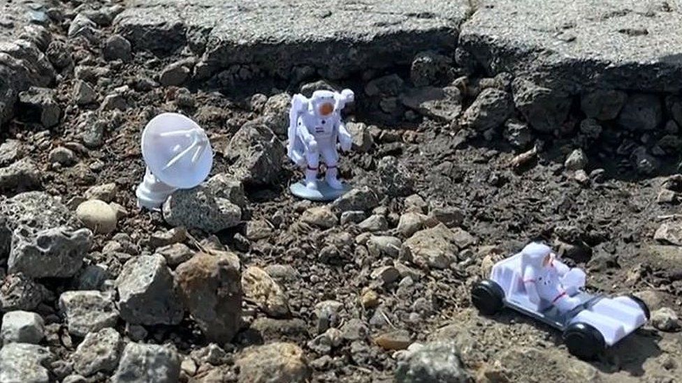 Small astronaut figures in a pothole