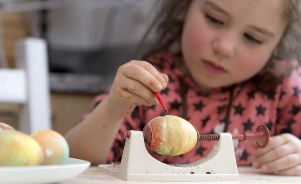 A young girl paints a marbled egg held still in a vice