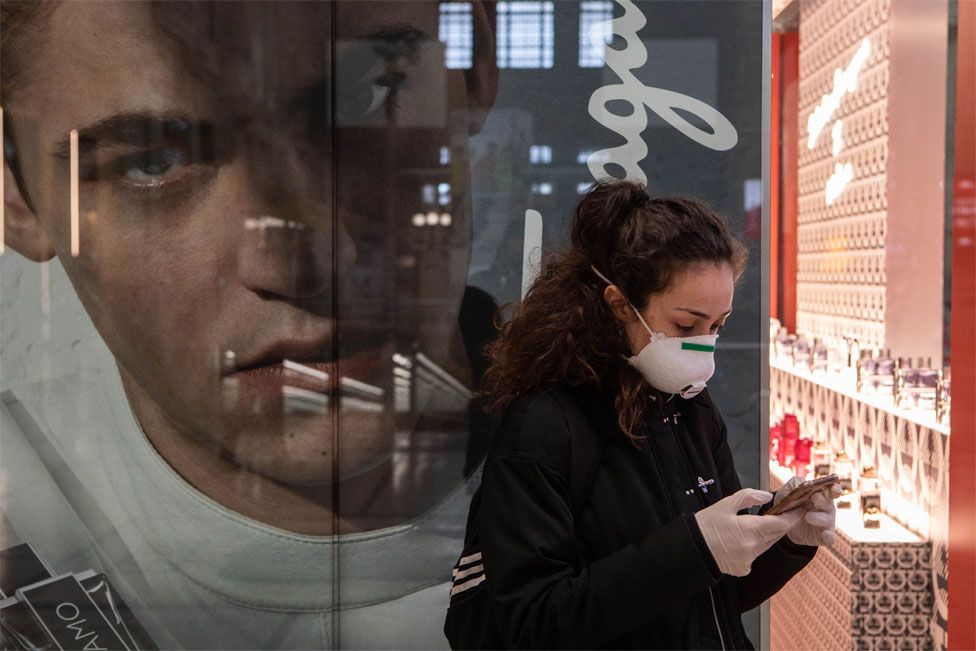 A woman checks her mobile phone with a large advertising poster of a face behind her