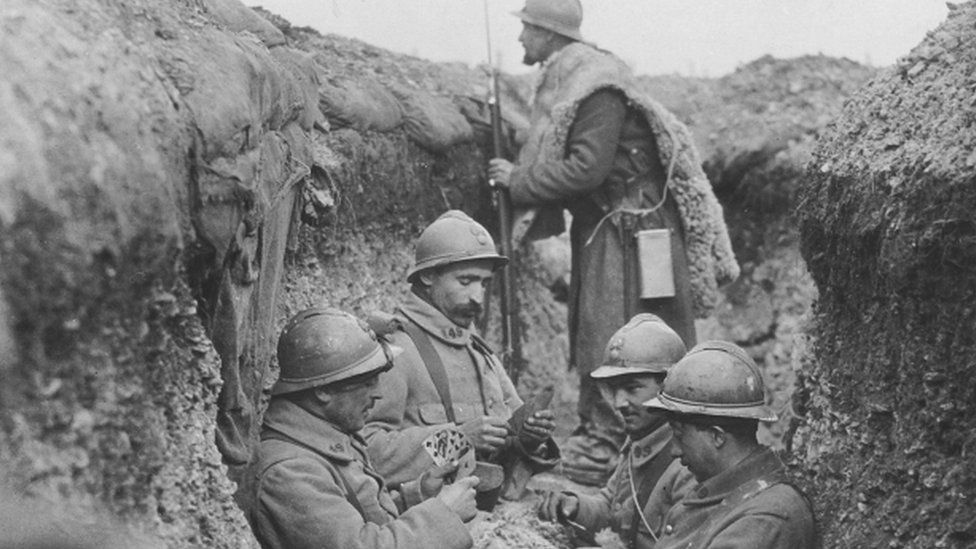 French soldiers warmly dressed in sheepskins play cards while manning a trench